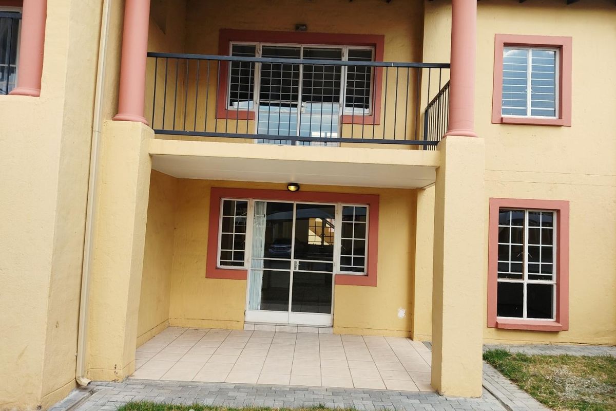 Rear view of an apartment building featuring a ground-floor tiled patio and an upper-level balcony with security bars and sliding glass doors.