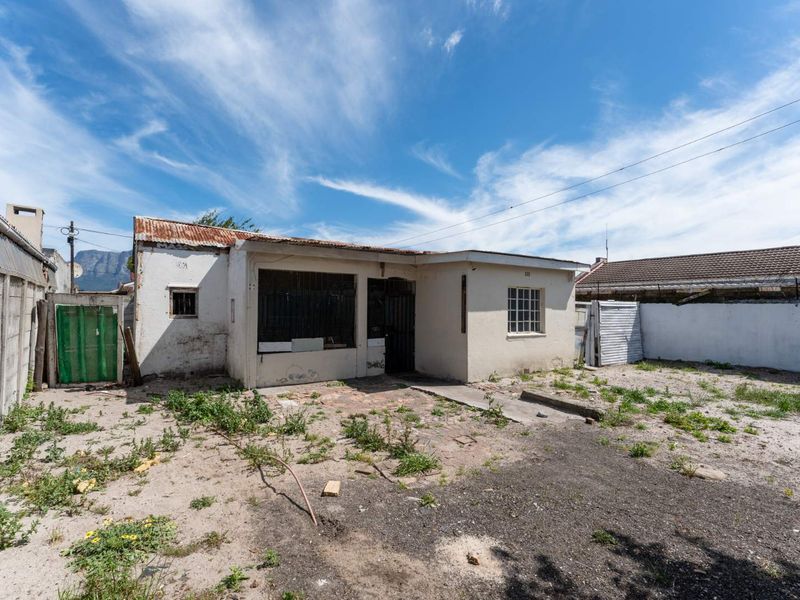 Rear view of a property featuring a corrugated metal roof, security bars, and a large yard area in need of significant maintenance and landscaping.