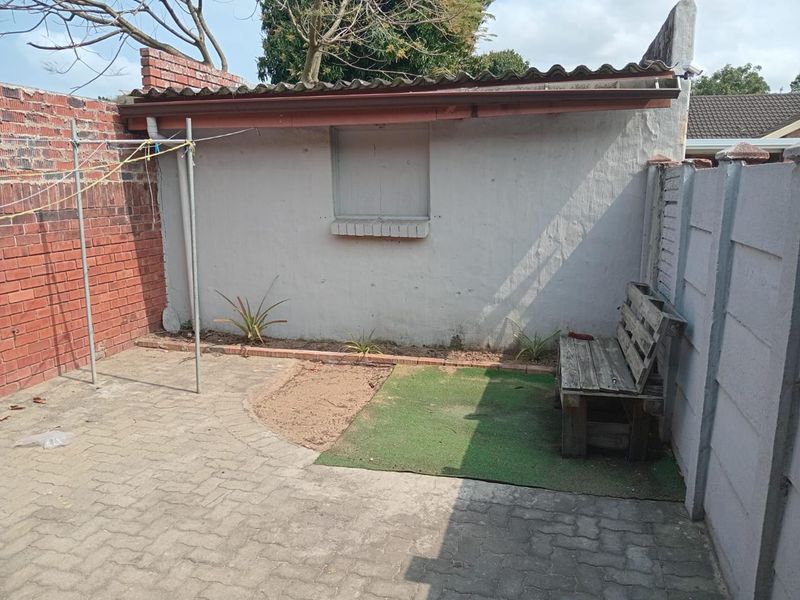 A private rear courtyard featuring paved flooring, brick and precast boundary walls, and a small garden area with a fixed window shutter.