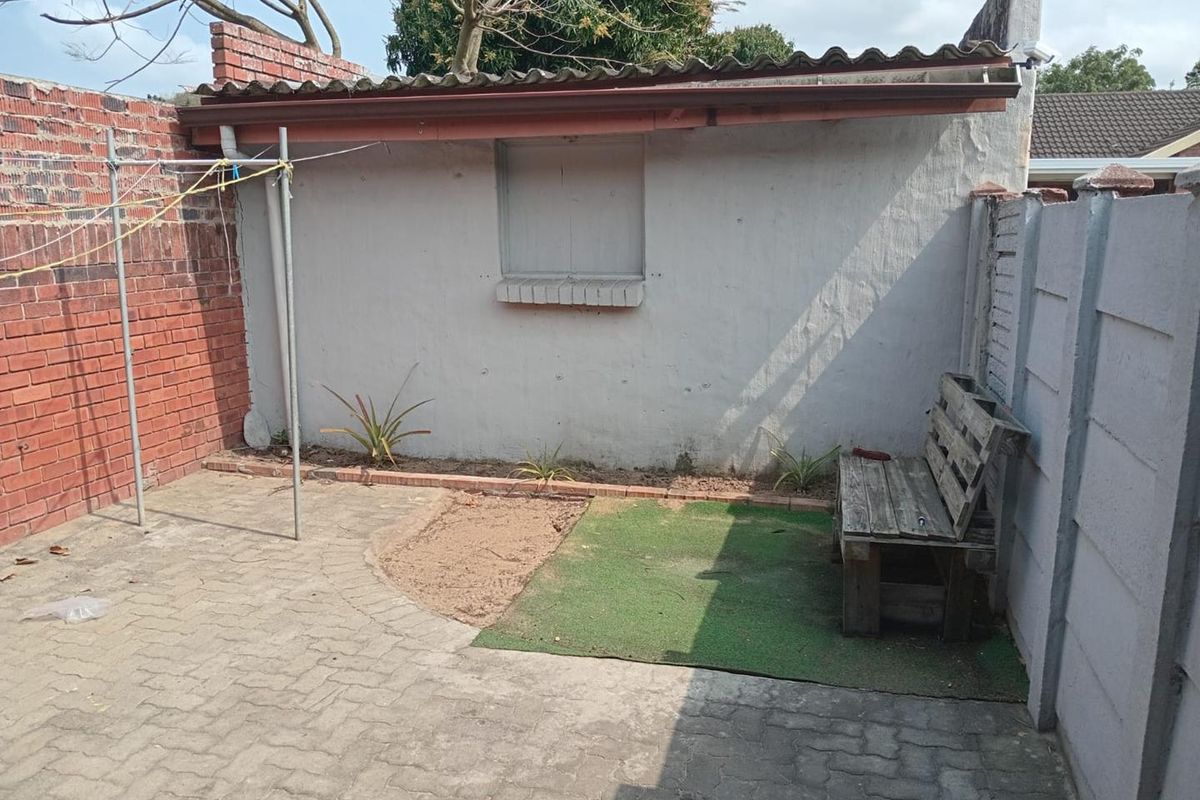 A private rear courtyard featuring paved flooring, brick and precast boundary walls, and a small garden area with a fixed window shutter.