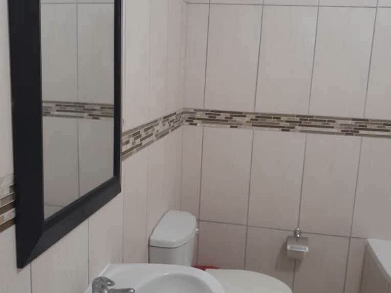 A functional bathroom featuring tiled walls with a decorative border, a wall-mounted basin, and a standard toilet.