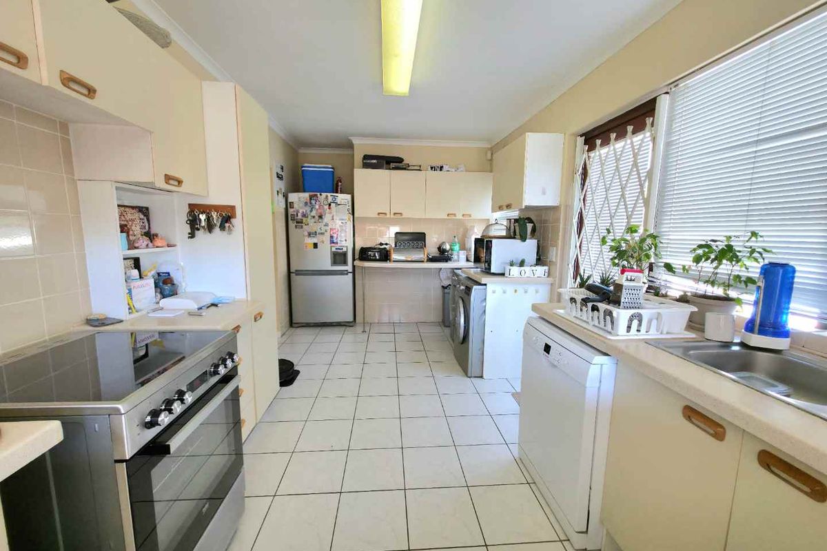 A functional kitchen featuring tiled flooring, laminate cabinetry, a freestanding oven, and integrated laundry facilities with a dedicated washing machine space.