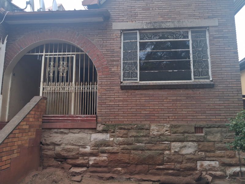 Front elevation of a brick house featuring a stone foundation, arched entrance with security gate, and classic casement windows with decorative security bars.