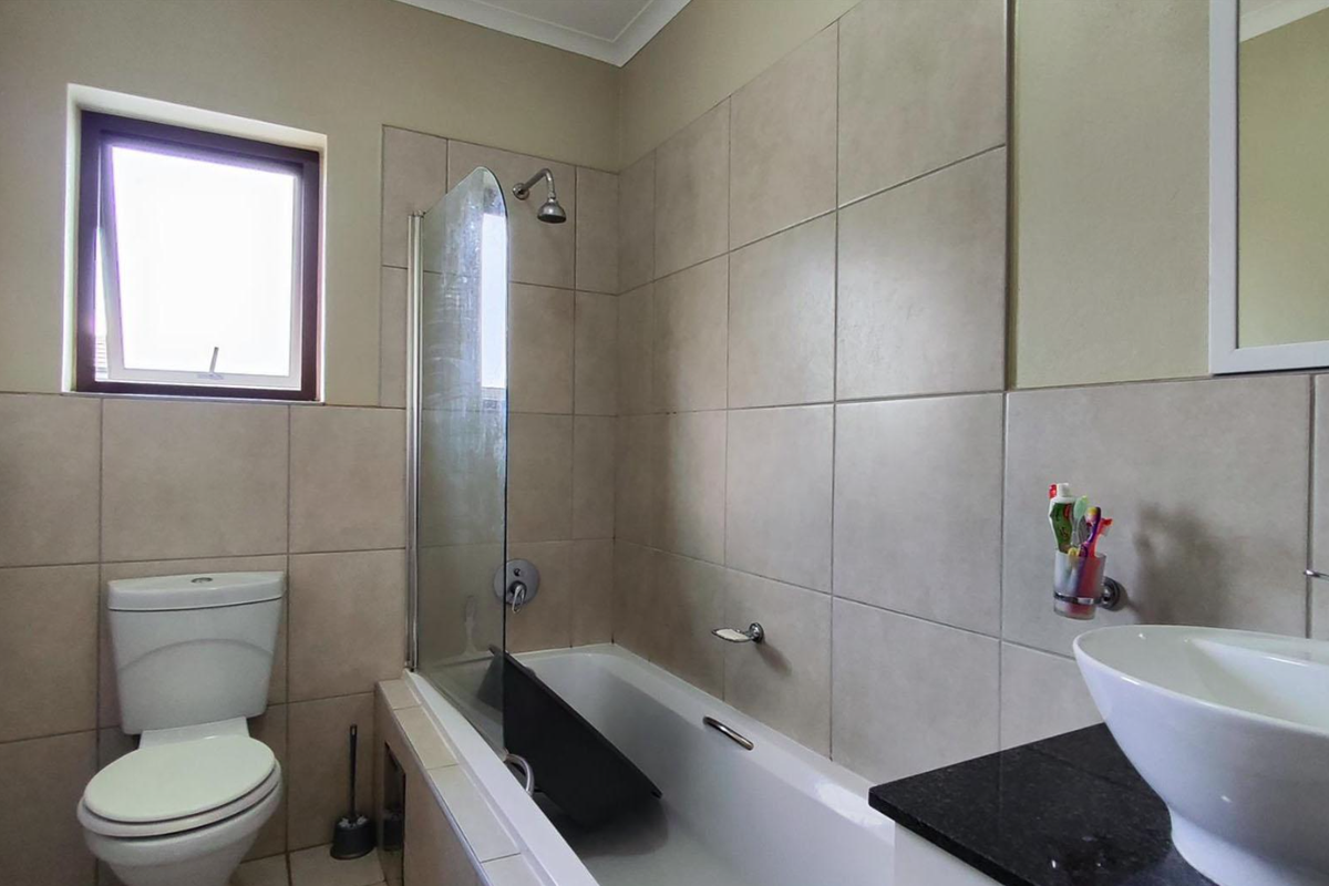 A functional bathroom featuring a bathtub with a glass shower screen, a wall-mounted basin with a granite vanity top, and a standard toilet.