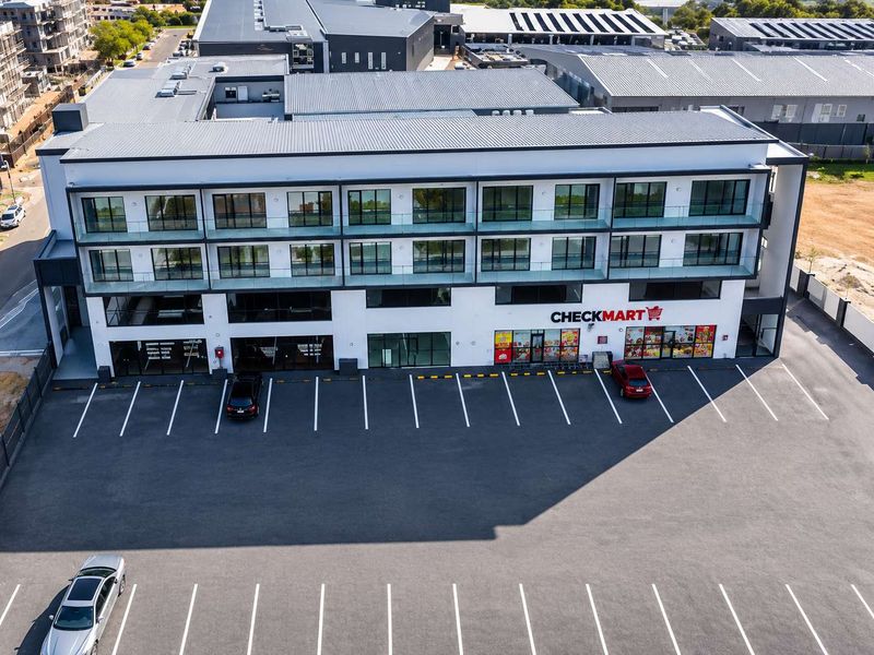 Aerial view of a modern multi-story commercial office and retail building featuring a large paved parking area and contemporary architectural design.