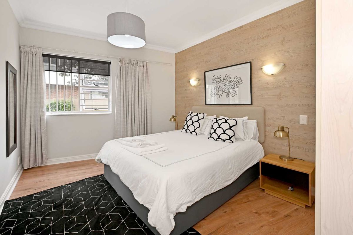 A well-maintained bedroom featuring wood-look flooring, a decorative feature wall, and a window with security bars.