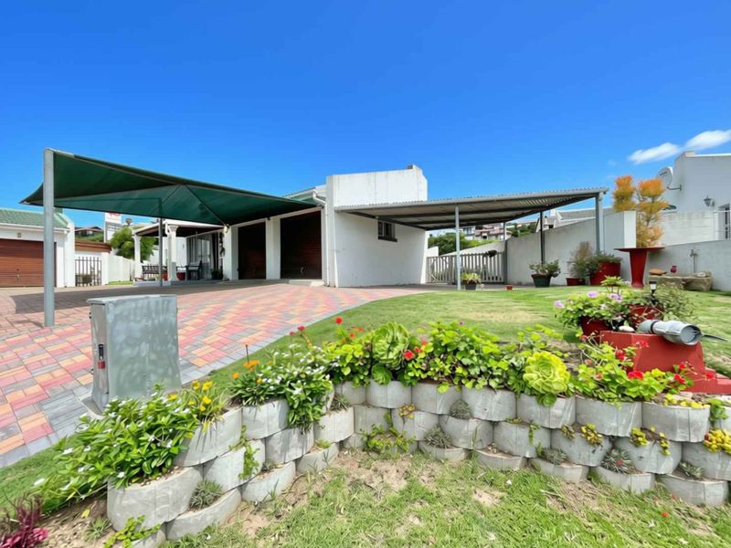 Front exterior view of the property featuring a paved driveway, dual carport structures, and a landscaped garden with a tiered retaining wall.