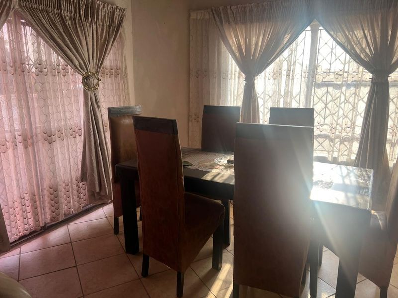 A dining room featuring ceramic floor tiles, a sliding glass door, and a security gate, with natural light entering through the windows.