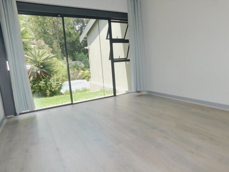 A bright, empty bedroom featuring light-toned laminate flooring and a large sliding glass door providing direct access to the garden and pool area.