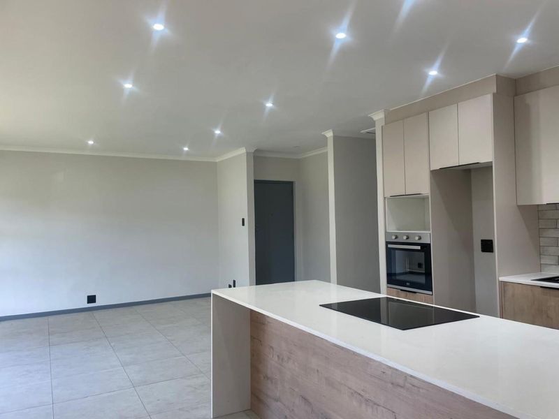 Modern open-plan kitchen and living area featuring a central island with induction hob, built-in oven, and neutral contemporary finishes.