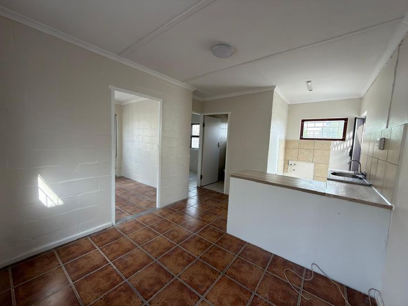 Open plan living and kitchen area featuring ceramic floor tiles, a breakfast bar, and a functional kitchen sink with tiled backsplash.