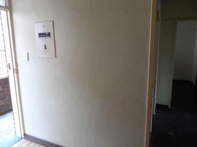 A view of a hallway featuring an electrical distribution board and tiled flooring, leading towards an exterior doorway.