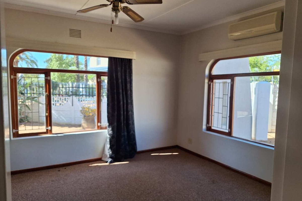 A spacious, empty bedroom featuring large windows with security bars, a ceiling fan, and a wall-mounted air conditioning unit.