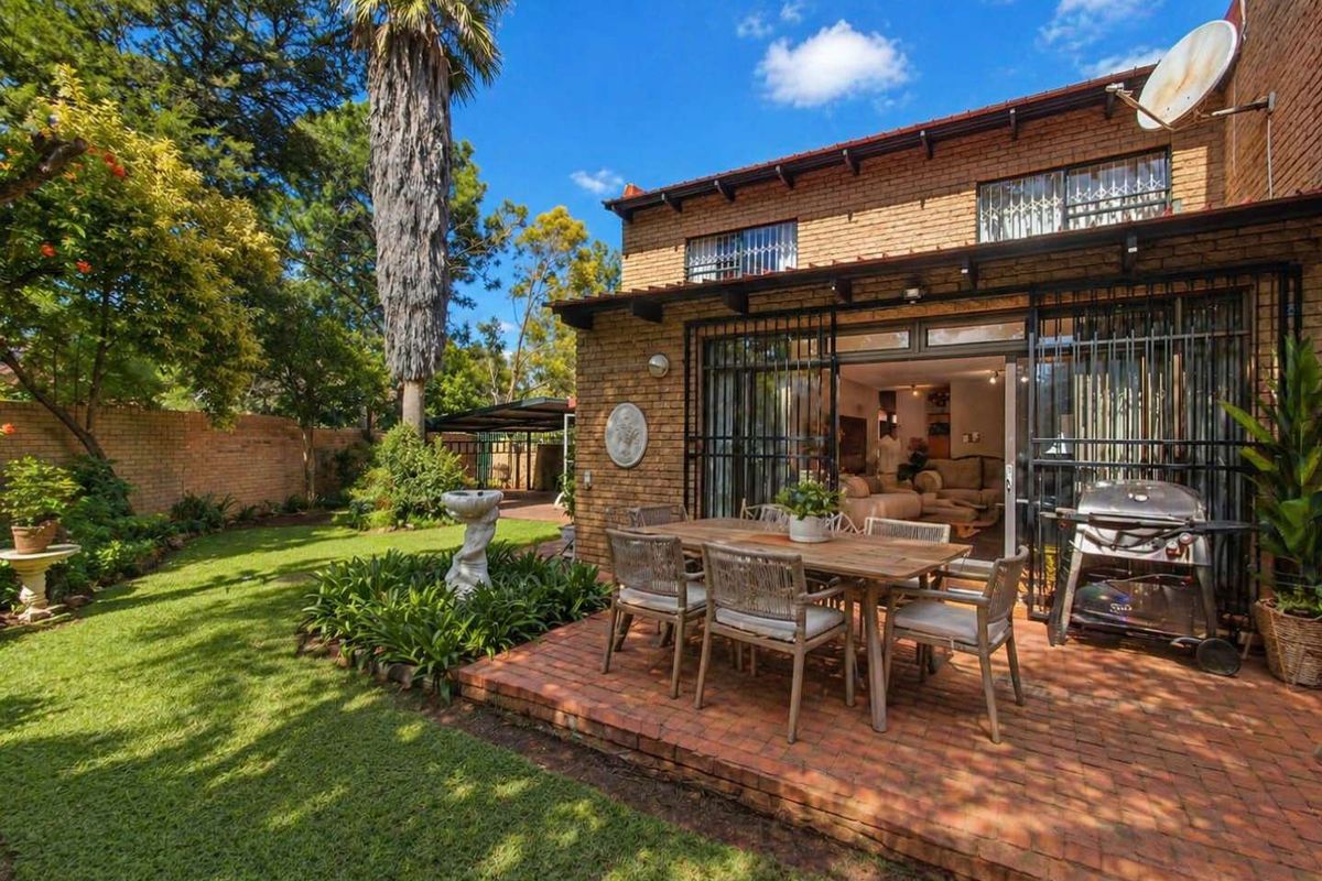 Rear view of the townhouse featuring a brick facade, a paved patio area, and a well-maintained private garden with mature trees.