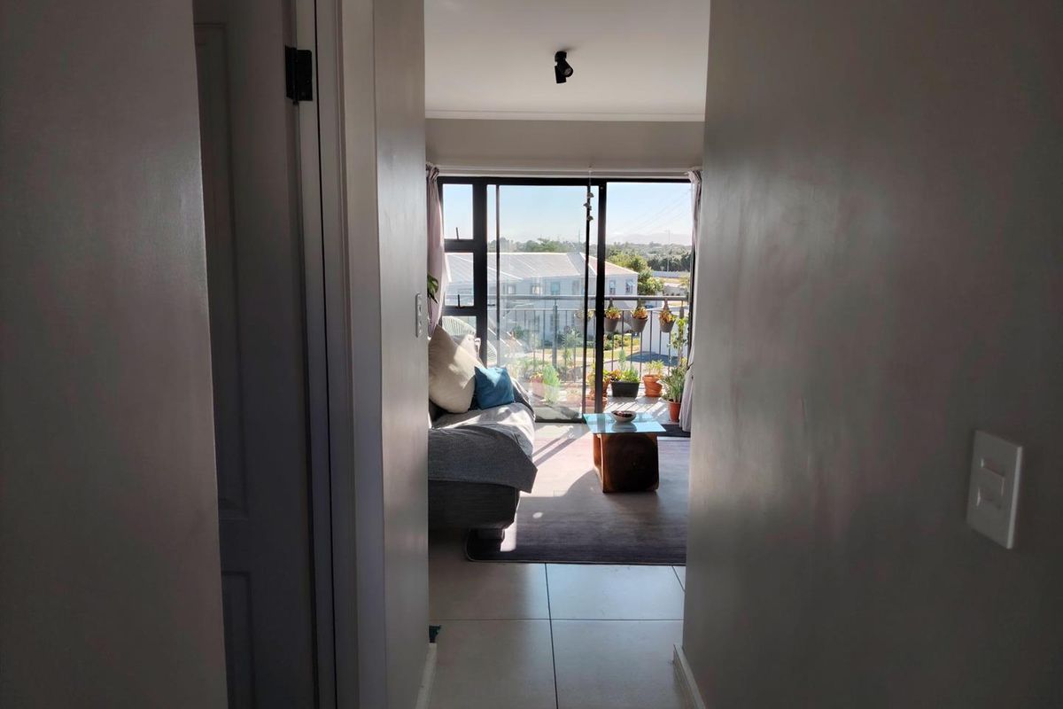 A view from the hallway into a bright living area featuring tiled floors and large sliding glass doors leading to a balcony.