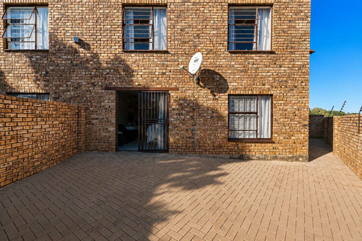 A rear exterior view of a face brick apartment building featuring a paved patio area and secure sliding door access.