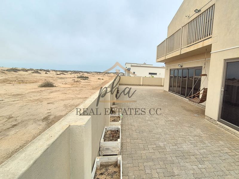 Spacious paved patio area featuring a boundary wall and direct access to the home through large sliding glass doors, overlooking a coastal landscape.