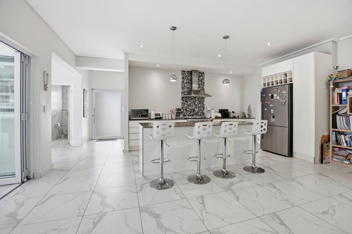 Modern open-plan kitchen featuring a central island, mosaic tile backsplash, sleek white cabinetry, and polished marble-look floor tiles.