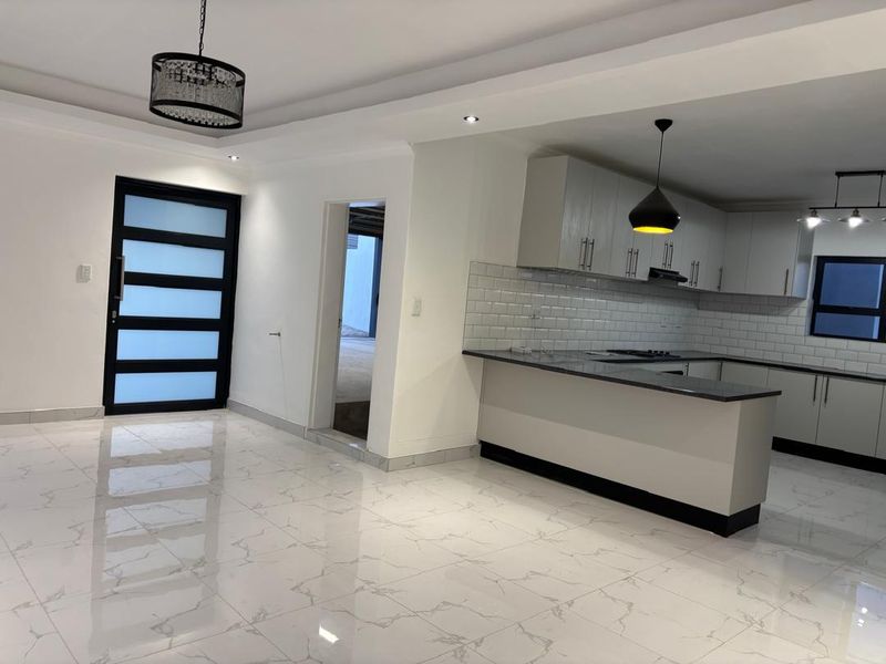 Modern open-plan living area featuring a sleek kitchen with subway tile backsplash, stone countertops, and high-gloss porcelain floor tiles throughout.