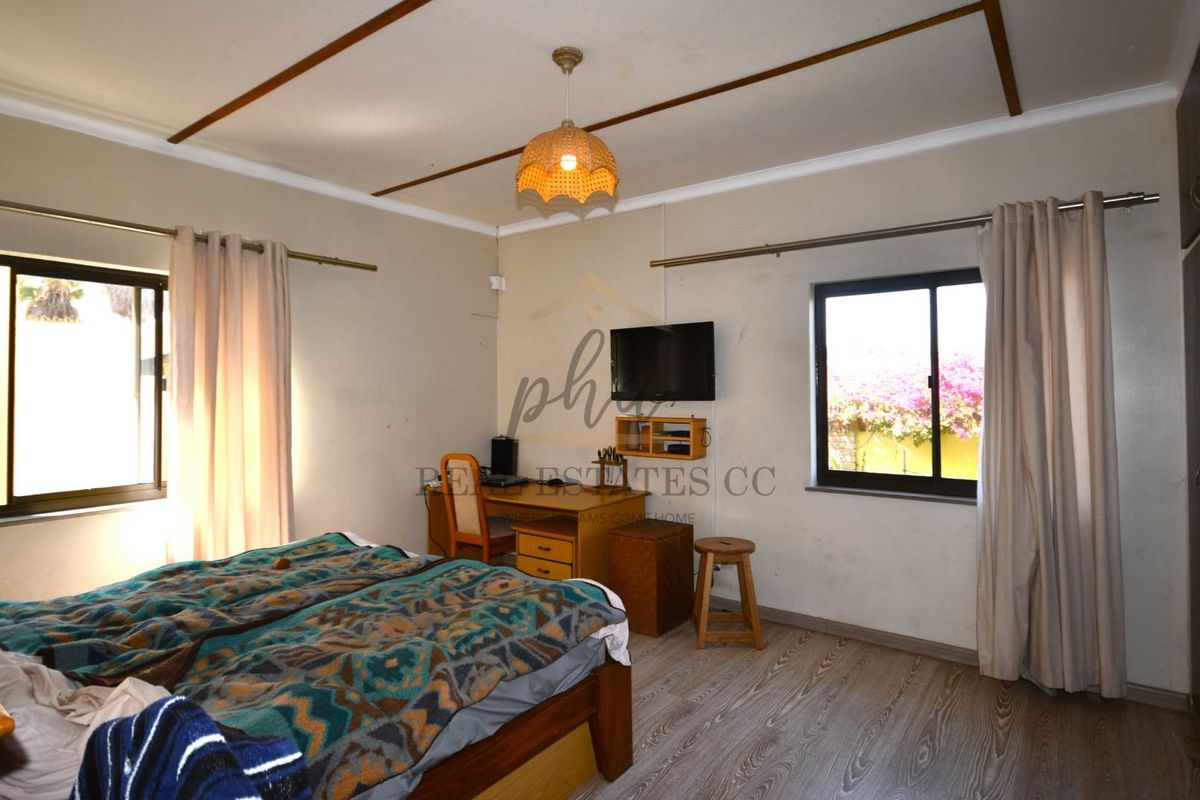 A spacious bedroom featuring wood-look laminate flooring, built-in wardrobe cabinetry, and dual windows providing natural light.