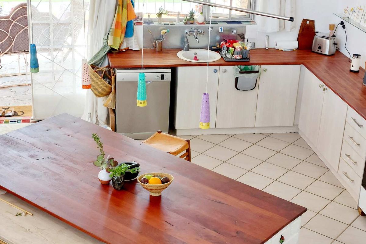 A functional kitchen featuring wooden countertops, white cabinetry, a stainless steel sink, and tiled flooring, with an integrated dining island.