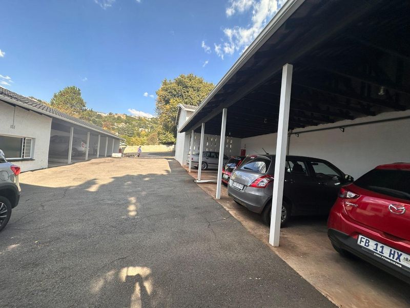 An open-air covered parking area with asphalt surfacing and structural support pillars for an apartment complex.