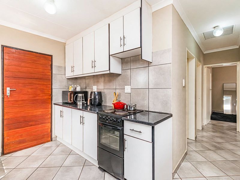 A functional kitchen featuring white cabinetry, dark countertops, tiled backsplash, and tiled flooring, with an adjacent hallway leading to other areas of the home.