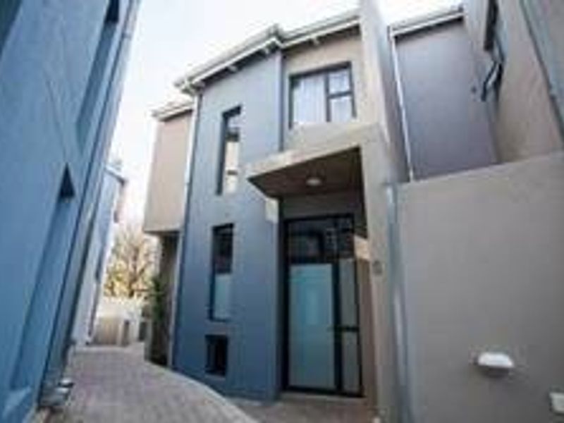 A modern townhouse exterior featuring a paved entrance path, contemporary facade with grey tones, and a glass-panelled front door.