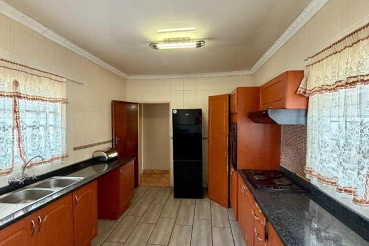 A functional galley-style kitchen featuring wood-tone cabinetry, granite countertops, a double basin sink, and integrated cooking appliances with tiled flooring.