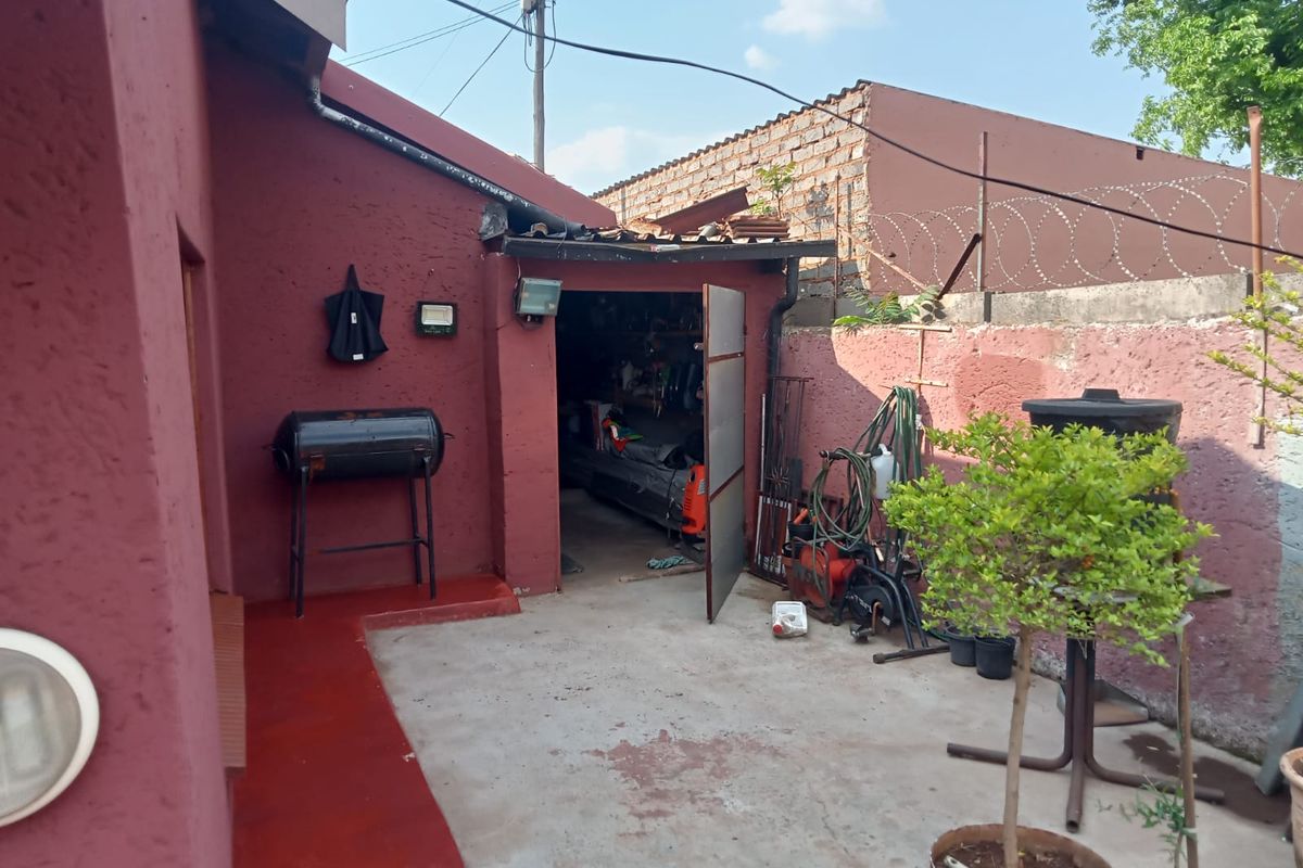 Rear exterior area featuring a concrete patio, boundary wall with security fencing, and access to a storage or utility space.