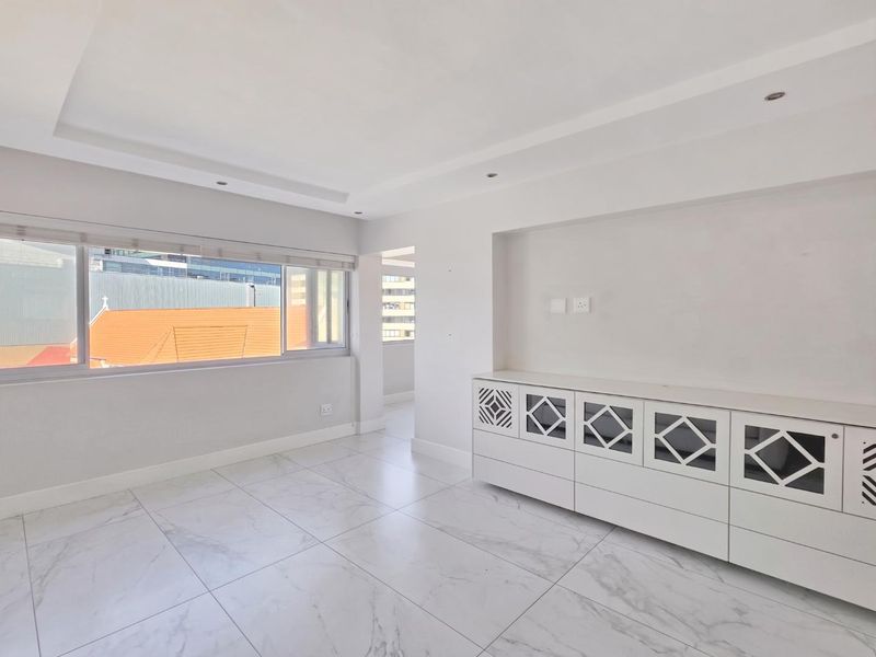 A bright, modern living area featuring marble-look floor tiles, recessed ceiling lighting, and custom built-in cabinetry with decorative fretwork panels.