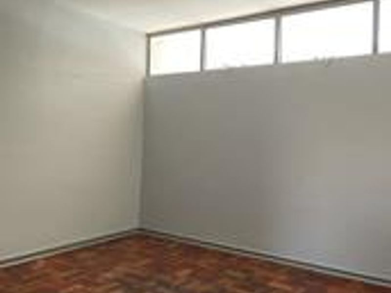 An empty bedroom featuring classic parquet flooring and high-level clerestory windows, providing a bright and neutral space ready for personalization.