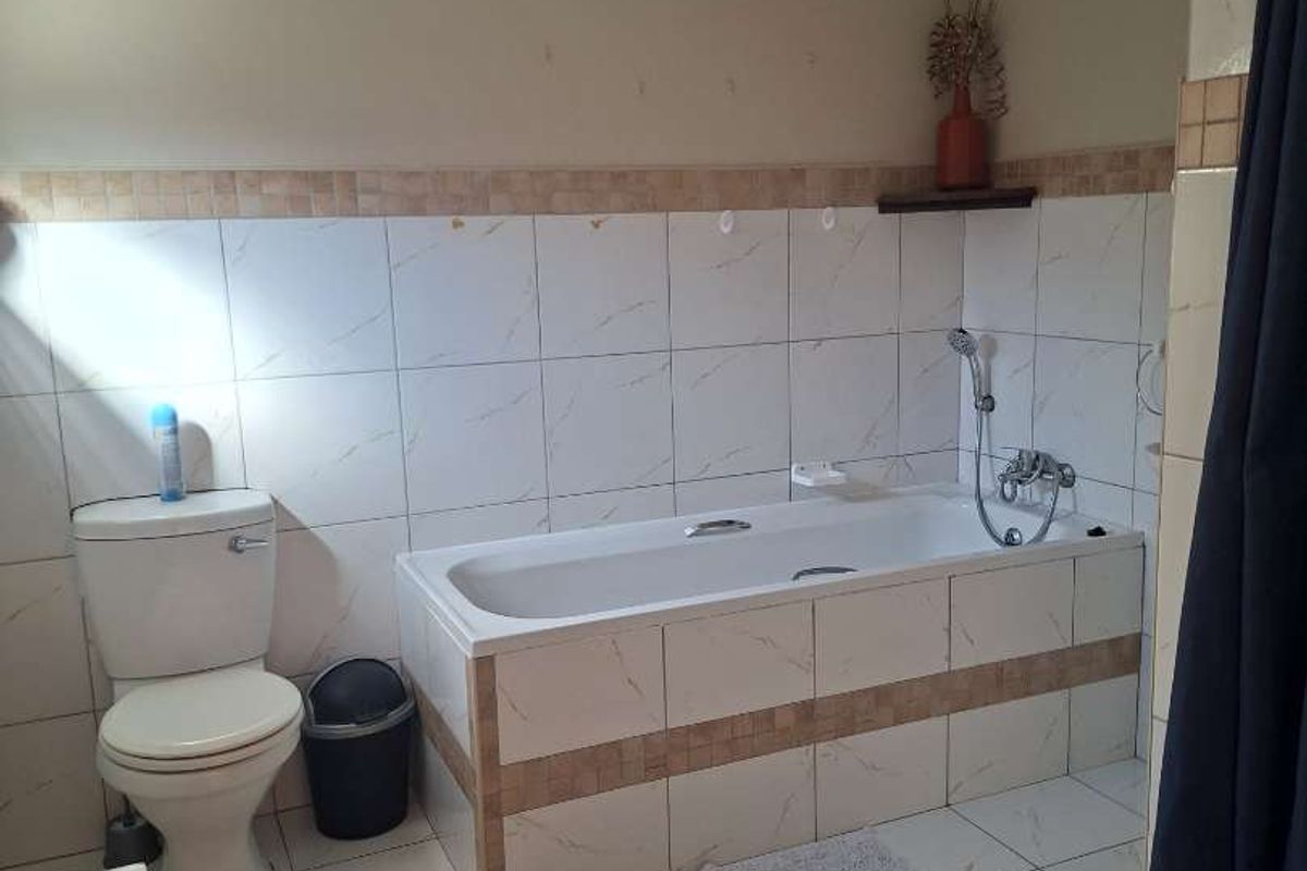 A functional bathroom featuring a built-in bathtub, toilet, and neutral wall and floor tiling throughout.