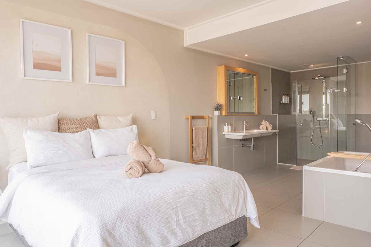 Modern open-plan bedroom featuring an integrated en-suite bathroom with a glass-enclosed walk-in shower, wall-mounted basin, and a built-in bathtub.