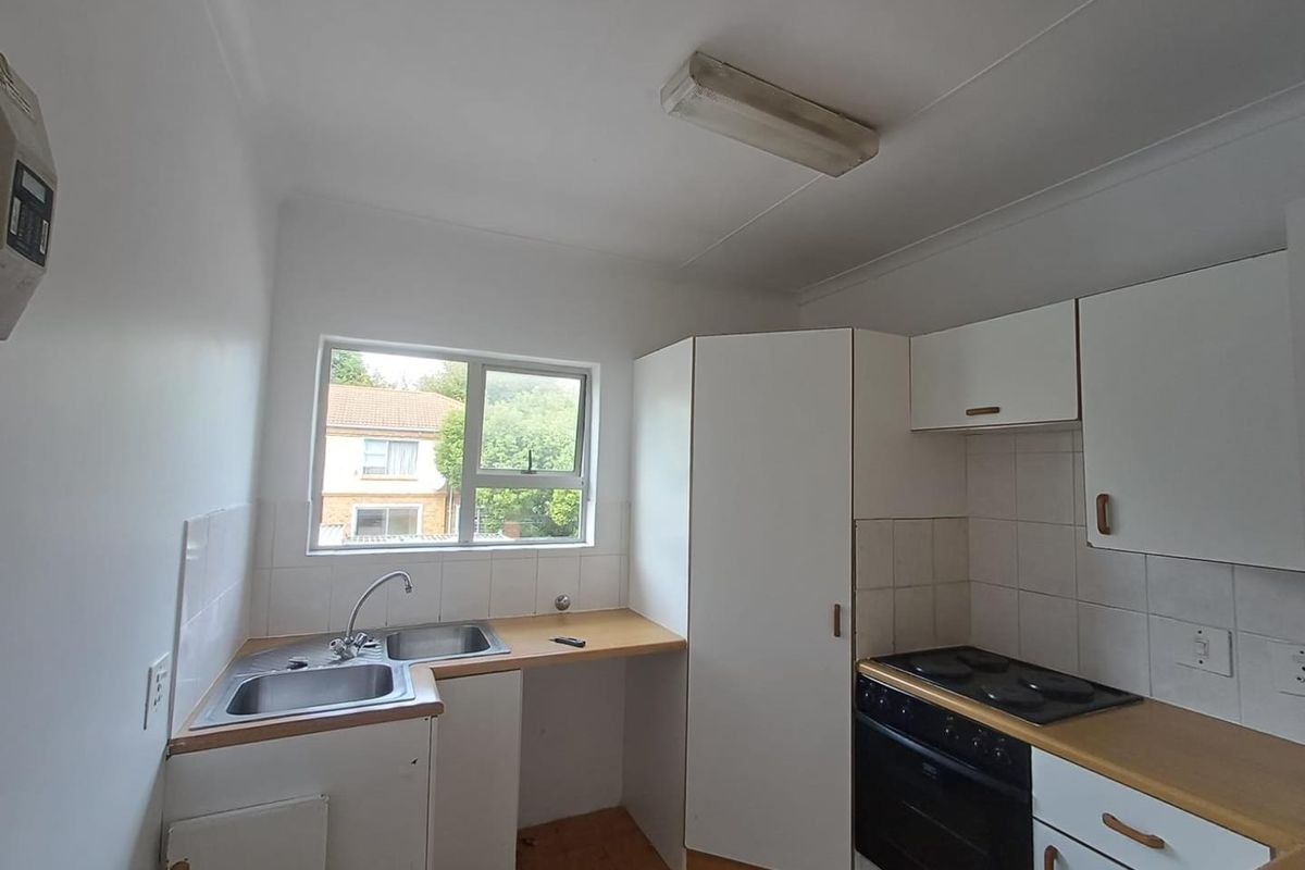 A compact, dated kitchen featuring white cabinetry, a built-in oven and hob, and a stainless steel sink with tiled splashbacks.