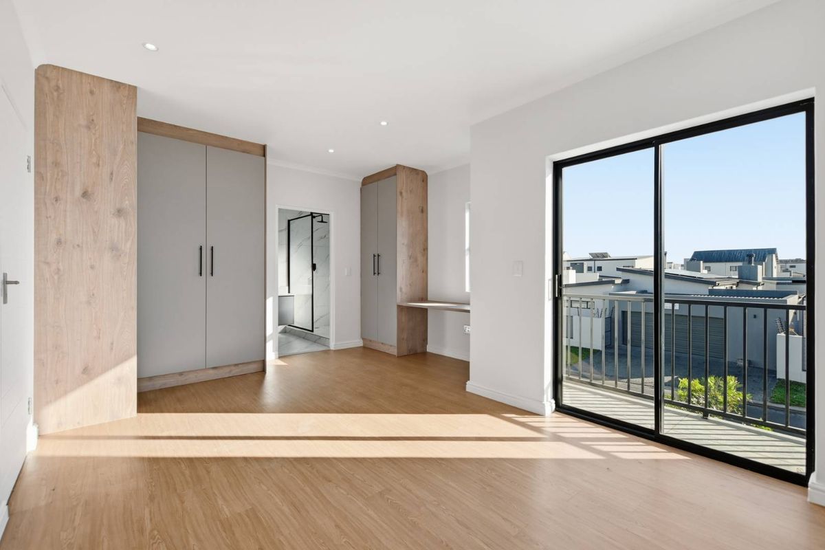 Spacious bedroom featuring modern built-in cupboards, an integrated desk, laminate flooring, and a sliding door leading to a private balcony.
