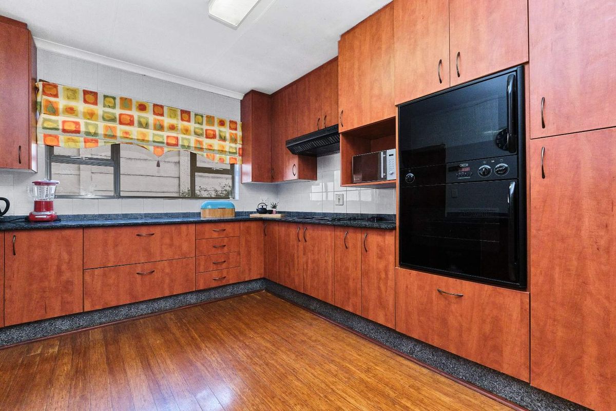 A functional kitchen featuring wood-look cabinetry, dark granite countertops, a built-in oven, and a black extractor fan.