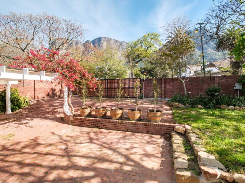 A spacious rear courtyard featuring brick paving, a pergola, and a stone retaining wall, set against a scenic mountain backdrop.