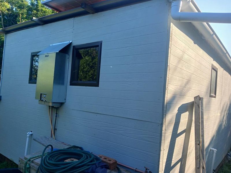 Exterior view of the rear building facade featuring timber-look cladding, a mounted gas geyser, and solar panel installation on the roof.