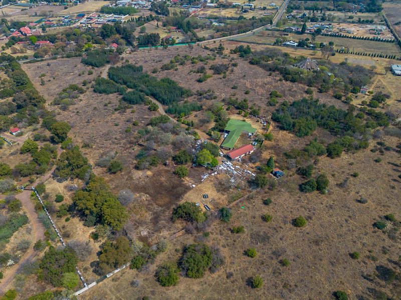 Aerial view of a large vacant residential land plot featuring existing structures, natural vegetation, and perimeter fencing.
