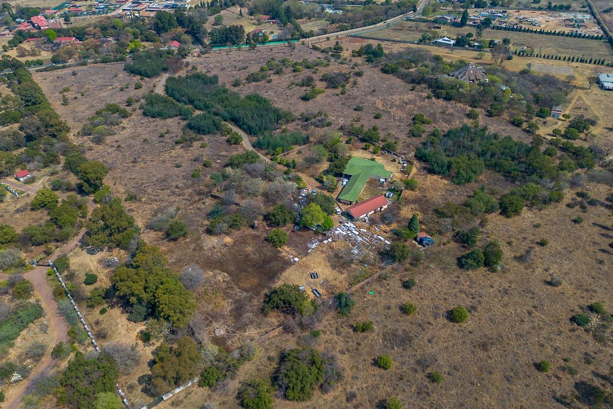 Aerial view of a large vacant residential land plot featuring existing structures, natural vegetation, and perimeter fencing.
