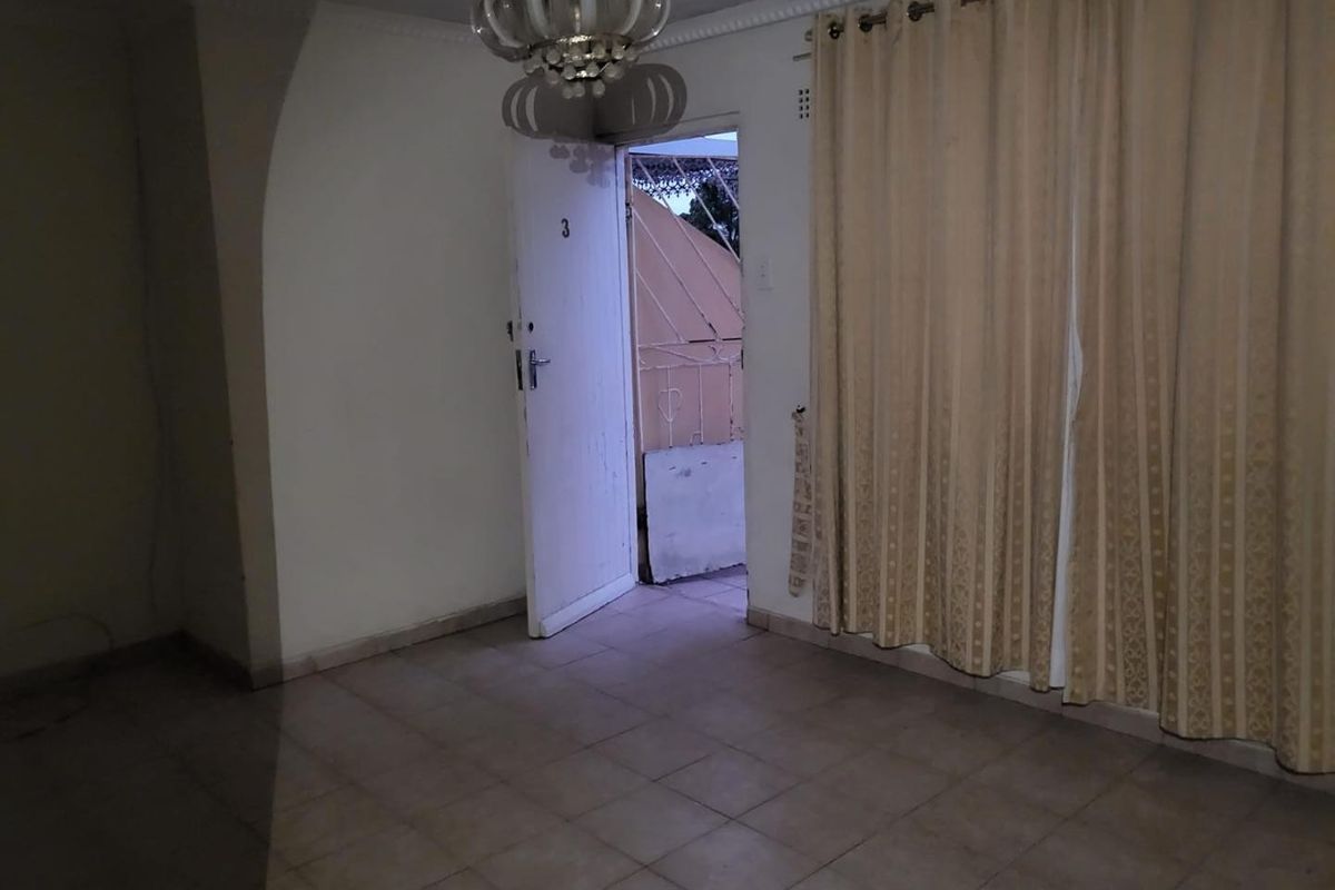 An empty living room area featuring tiled flooring and access to an outdoor balcony space, requiring cosmetic updates to improve its overall appeal.