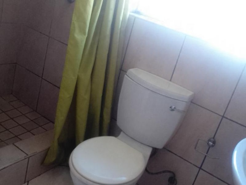 A functional bathroom featuring a toilet, shower area with tiled walls, and tiled flooring, providing a basic and practical layout.