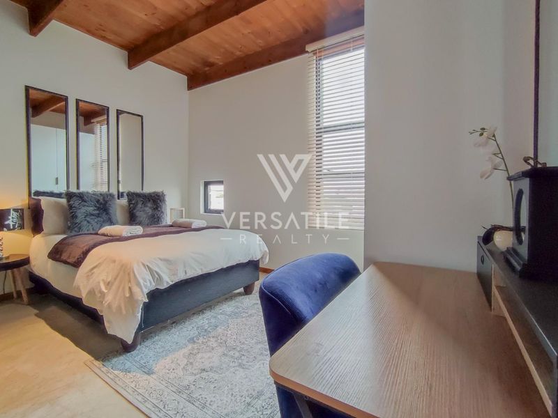 A well-lit bedroom featuring exposed timber ceiling beams, polished concrete flooring, and large windows with fitted venetian blinds.