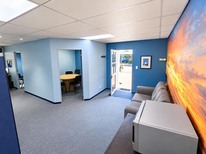 A bright office space featuring a suspended ceiling, carpeted flooring, and an adjoining meeting room with direct exterior access.