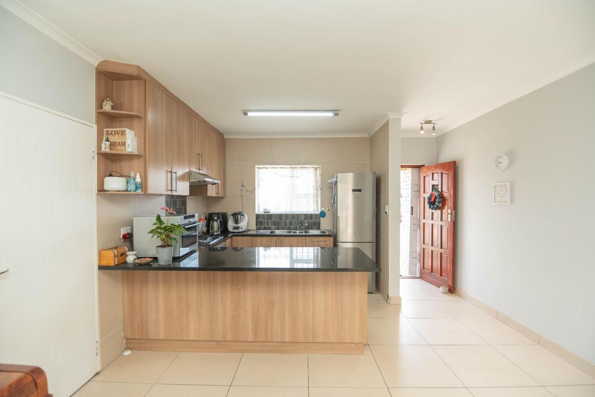 A functional kitchen featuring light wood cabinetry, dark granite countertops, a breakfast bar, and tiled flooring, with direct access to the exterior.