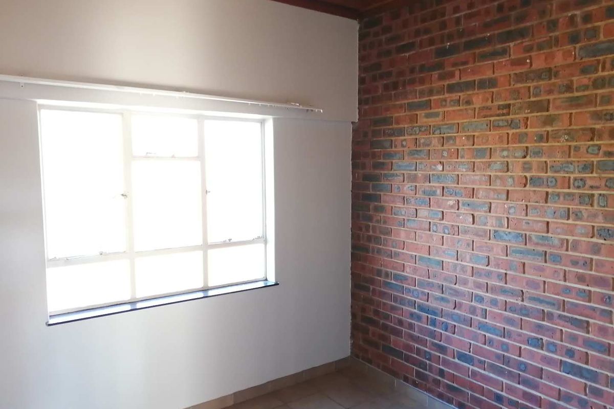 An empty bedroom featuring an exposed brick wall, tiled flooring, and a timber ceiling, offering a blank canvas for personalization.