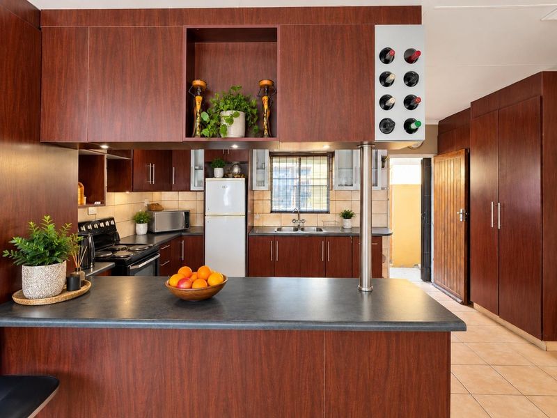 A functional kitchen featuring dark wood-look cabinetry, laminate countertops, a built-in wine rack, and tiled flooring with direct access to an exterior area.