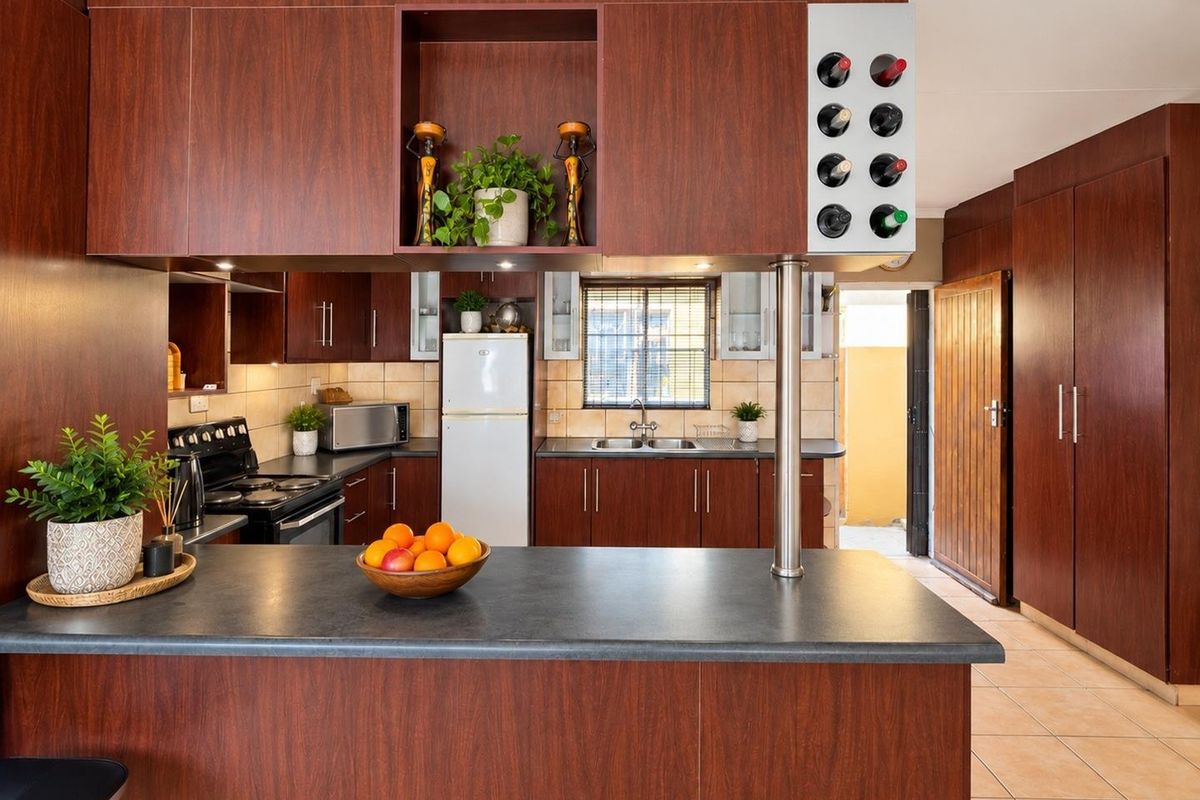 A functional kitchen featuring dark wood-look cabinetry, laminate countertops, a built-in wine rack, and tiled flooring with direct access to an exterior area.