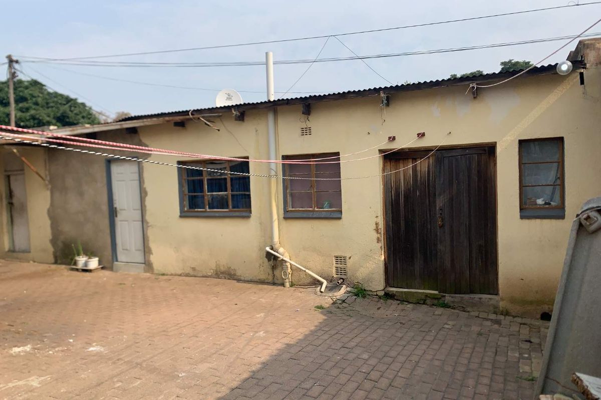 Rear exterior view of the property featuring a paved courtyard, weathered plaster walls, timber doors, and metal-framed windows under a corrugated iron roof.